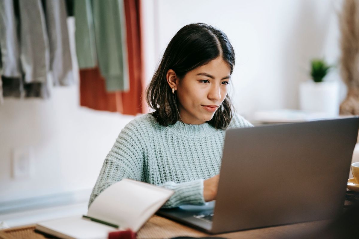 Una mujer joven toma notas junto a su computador, en su casa